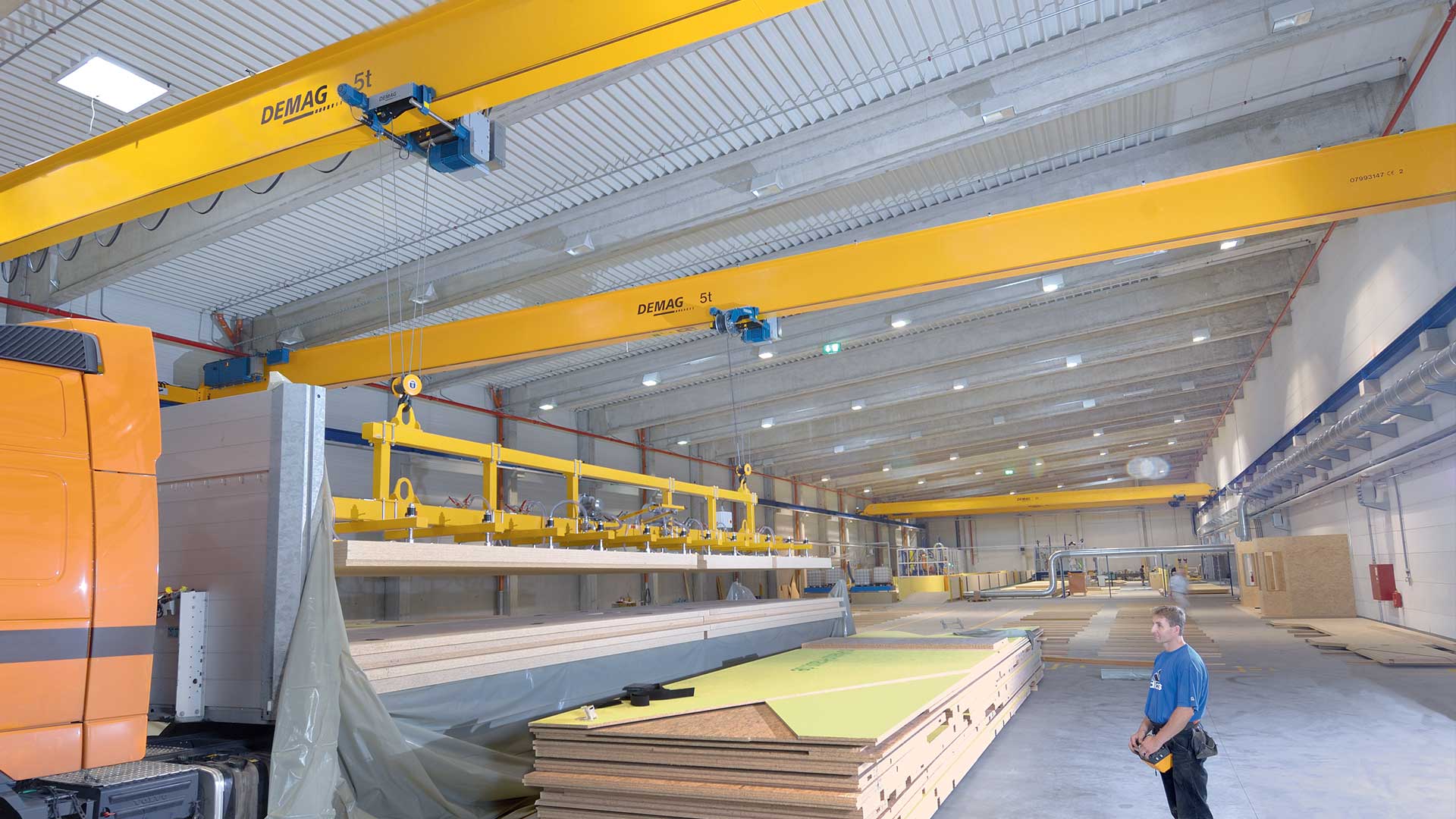 Demag hoists and cranes working in tandem to load wood products onto the bed of a truck.