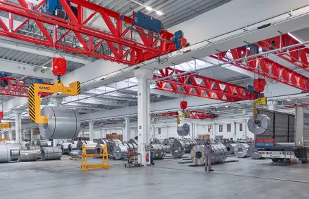 Demag double v-girder cranes lifting steel coils into a truck.