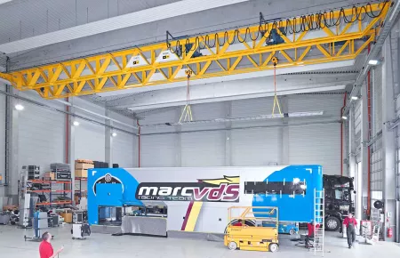 Demag double v-girder crane with 2 wire rope hoists synchronized to lift and transport a long load on one crane.