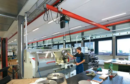 Operator using a Demag DC Com chain hoist to load a part into a machine.