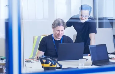 Zwei Mitarbeitende helfen sich gegenseitig an einem Computer bei einem Projekt in der Demag Research and Business Factory am Standort Wetter.