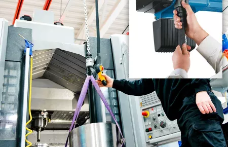 An operator using a DC Com chain hoist to place a large aluminum puck into a machine using the ergonomic pendant. There is an inset picture of someone easily adjusting the pendant length on a DC Com.