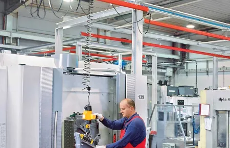 Machine operator using a Manulift chain hoist to load a part with one hand controlling the handle.